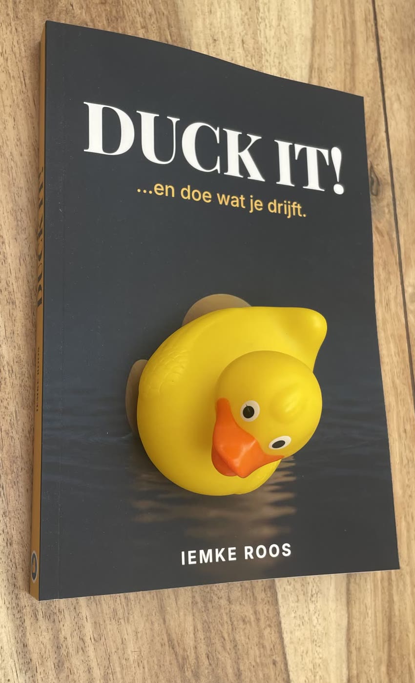 Het gedrukte boek Duck It! op een houten tafel, met de echte badeend van de omslag er middenop